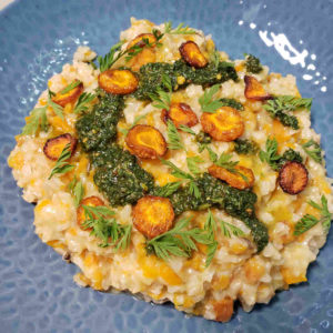 Roasted carrot risotto plated with carrot top pesto, roasted carrot "coins" and some chopped carrot greens.