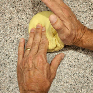 Holding the dough ball in place with one hand, use the other palm to lift one side of the dough ball and...